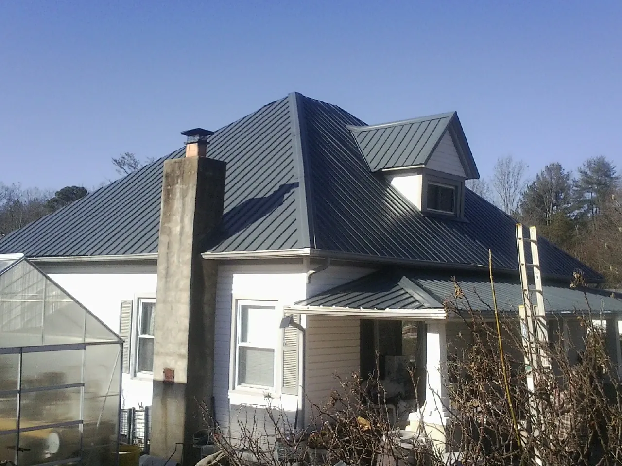 Dark blue standing seam metal roof on a white farmhouse with dormer — Slate & Tile Roof Repair by Roofing Brothers in Round Mountain